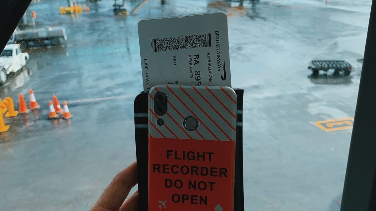 Traveler holding a boarding pass with a plane visible through the window at Keflavík Airport