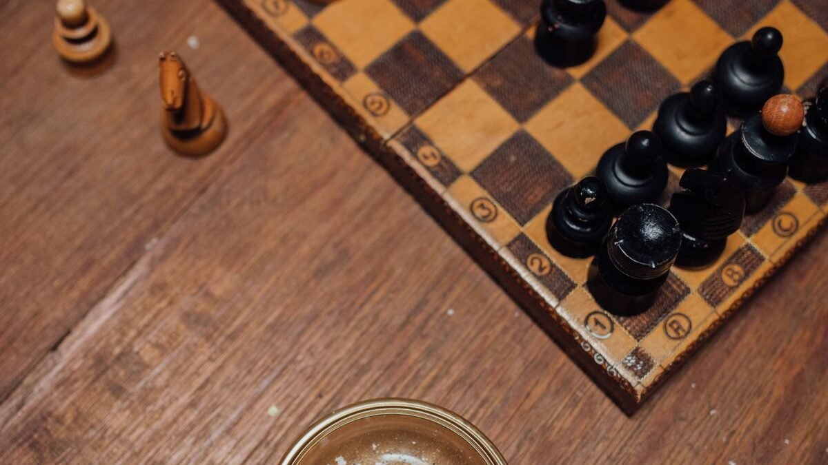 Detailed view of a chessboard with a glass ashtray containing cigarette butts on a wooden table.