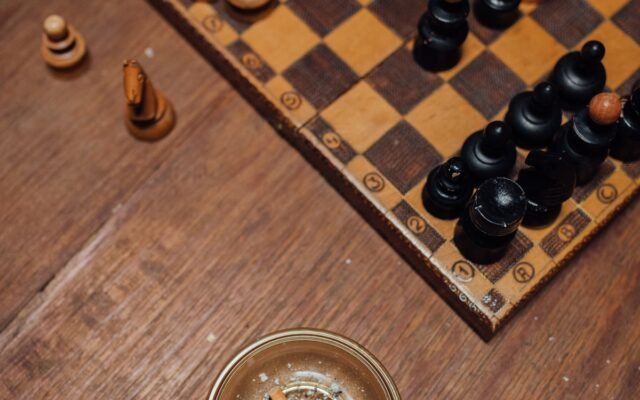 Detailed view of a chessboard with a glass ashtray containing cigarette butts on a wooden table.