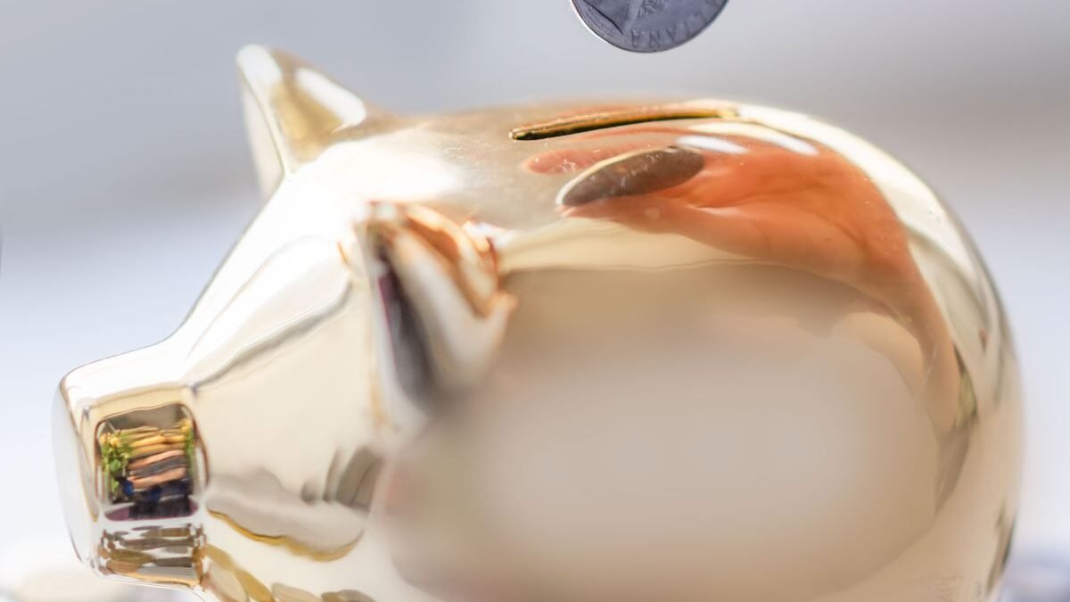 Hand placing coin into a golden piggy bank surrounded by coins
