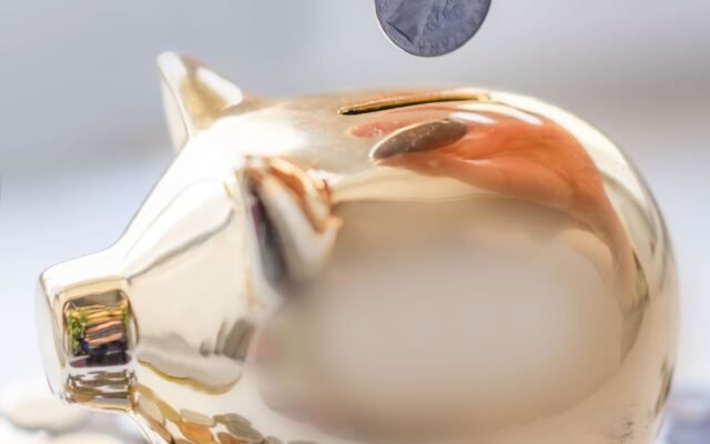 Hand placing coin into a golden piggy bank surrounded by coins