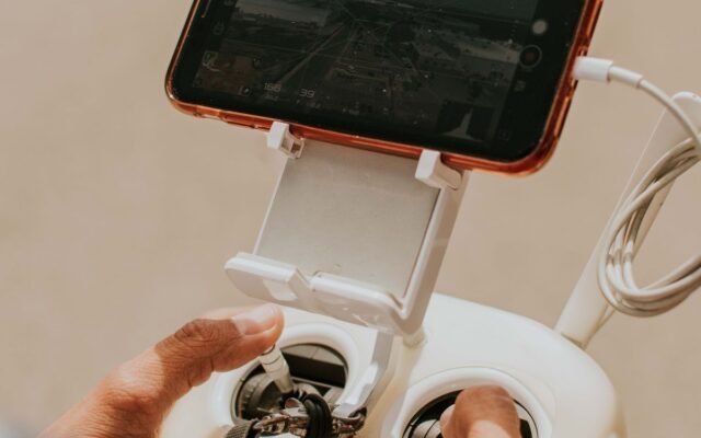 Hands holding a drone controller connected to a smartphone