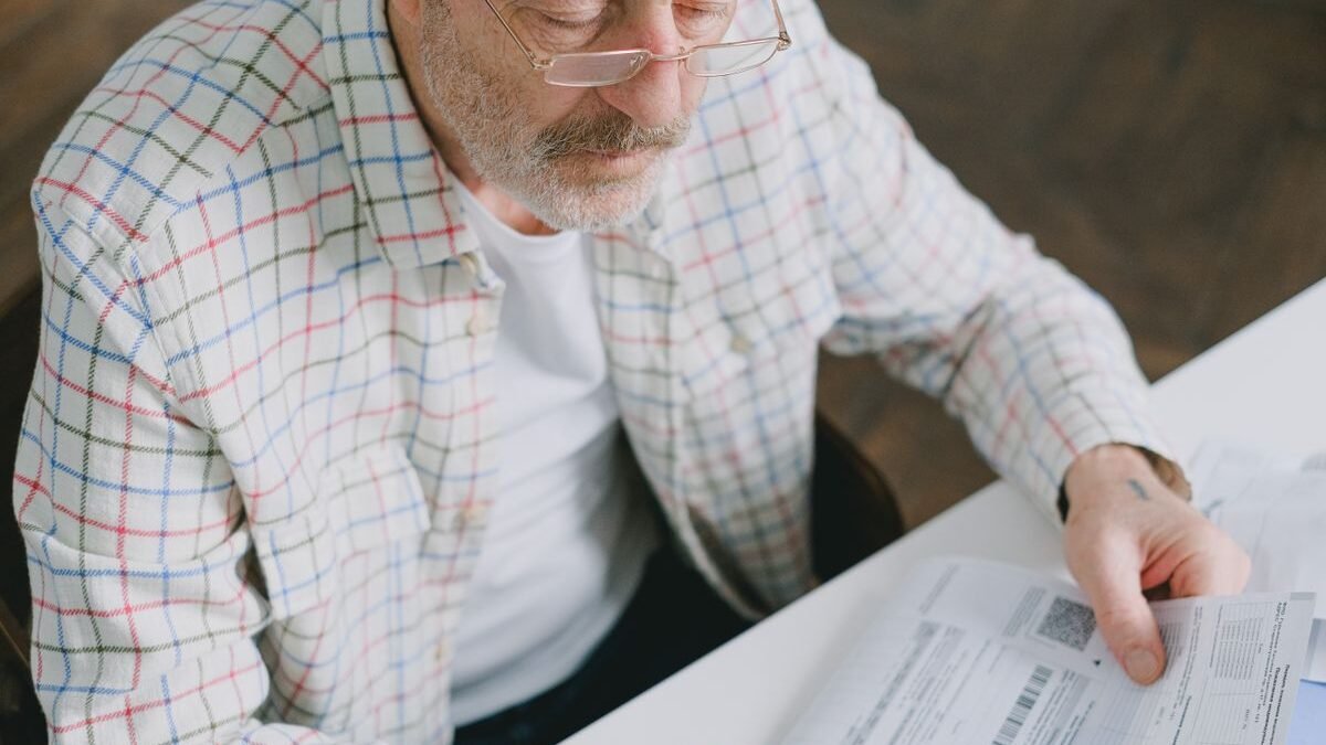 Elderly man in glasses carefully examines documents at home. Thoughtful and focused