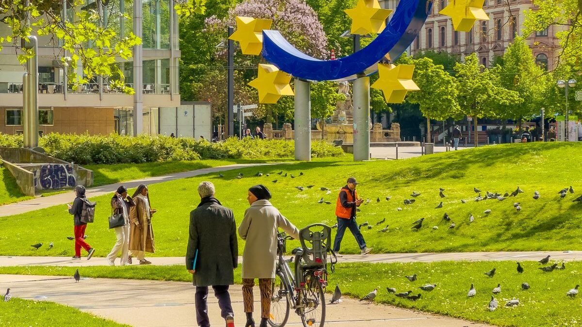 People walking near the iconic Euro sculpture in a sunny Frankfurt park
