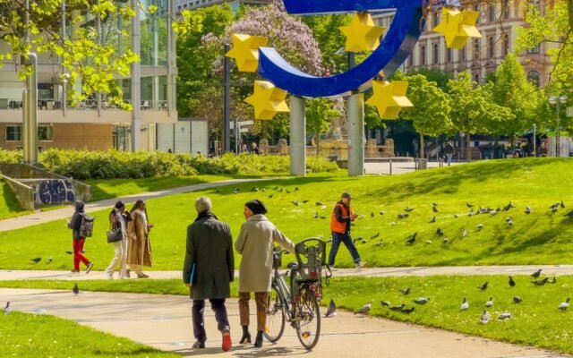 People walking near the iconic Euro sculpture in a sunny Frankfurt park