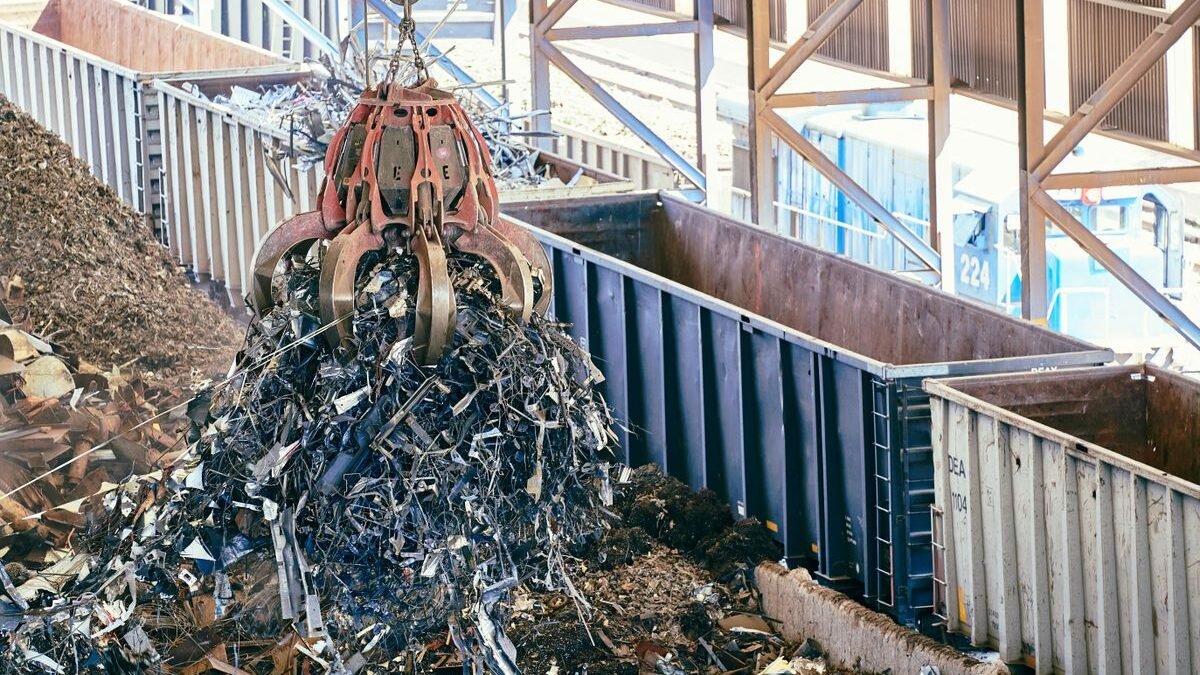 An industrial claw crane lifts metal scrap in a recycling facility