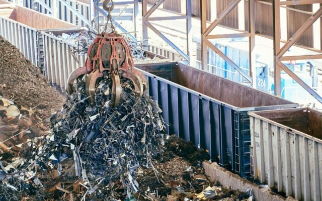 An industrial claw crane lifts metal scrap in a recycling facility