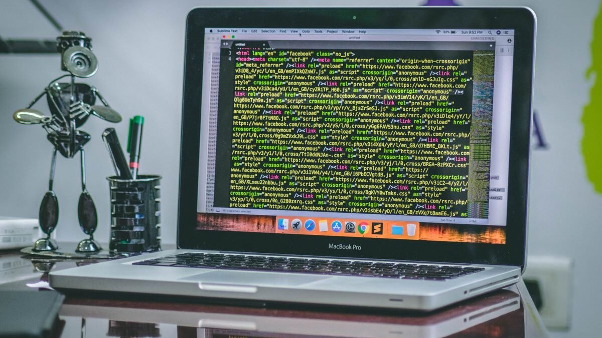 A sleek MacBook Pro displaying code on a desk with office tools and creative decorations