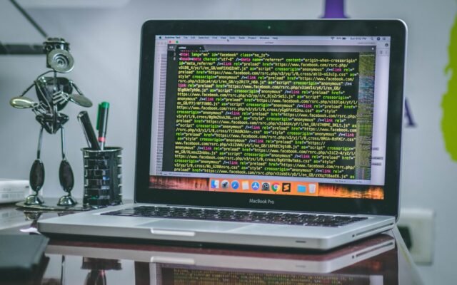 A sleek MacBook Pro displaying code on a desk with office tools and creative decorations
