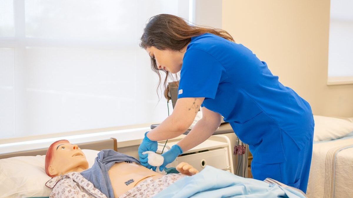 A nurse in blue scrubs practicing medical procedures on a hospital training manikin
