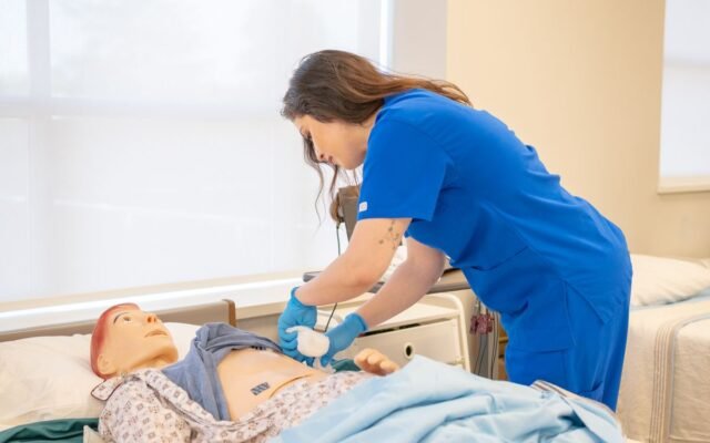 A nurse in blue scrubs practicing medical procedures on a hospital training manikin