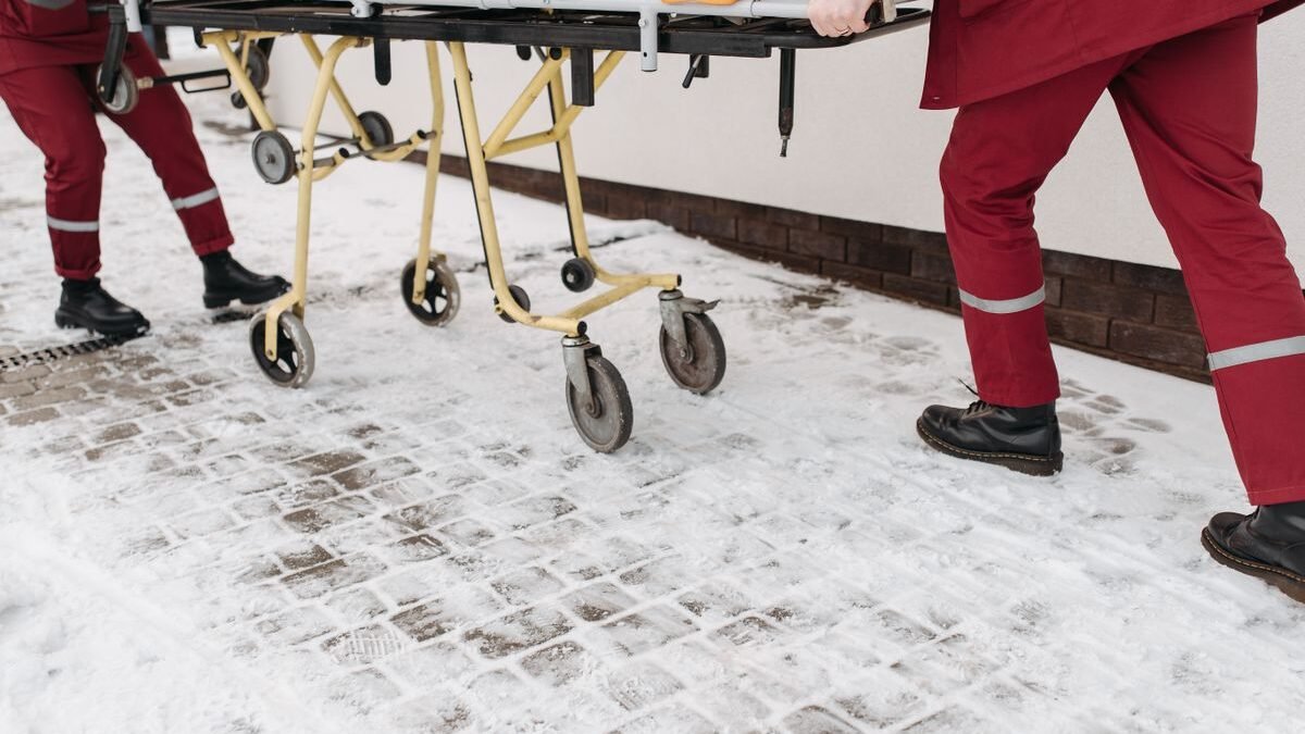 Two paramedics moving a stretcher across a snow-covered surface outdoors