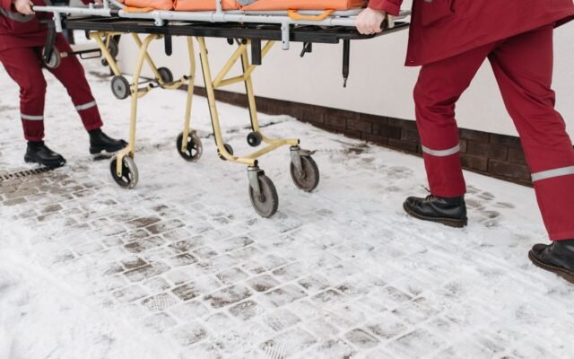 Two paramedics moving a stretcher across a snow-covered surface outdoors