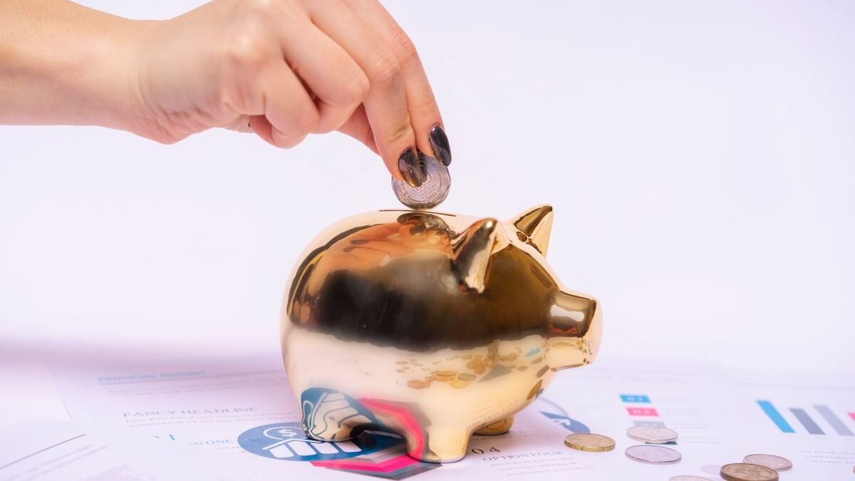 A hand places a coin into a golden piggy bank surrounded by financial documents
