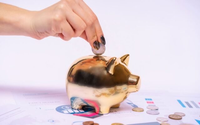 A hand places a coin into a golden piggy bank surrounded by financial documents