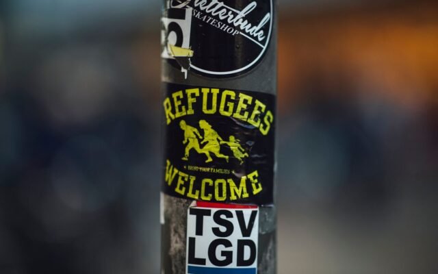 Street pole with stickers including 'Refugees Welcome'
