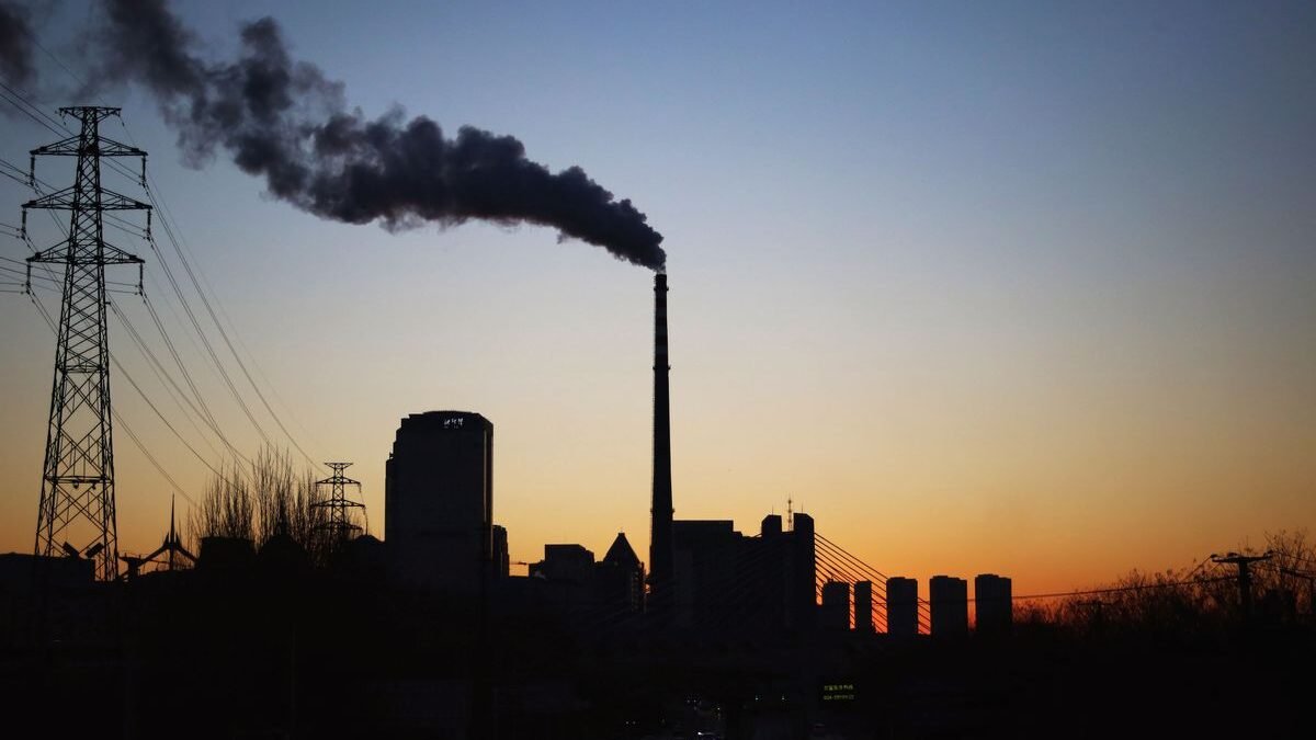Dramatic sunset silhouette of an industrial smokestack with pollution in the urban skyline