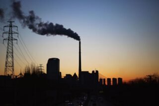 Dramatic sunset silhouette of an industrial smokestack with pollution in the urban skyline