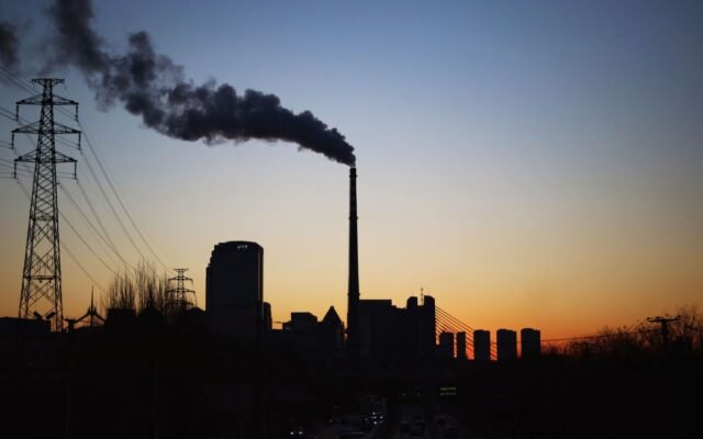 Dramatic sunset silhouette of an industrial smokestack with pollution in the urban skyline