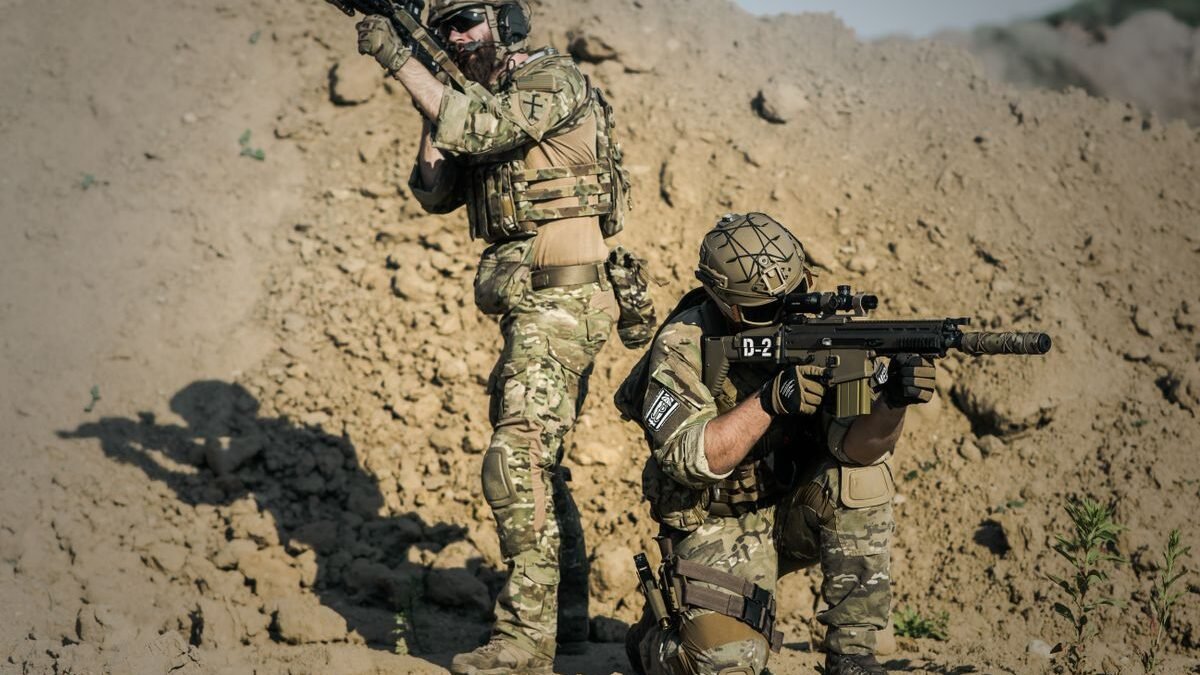 Two soldiers in camo engage in tactical training in a desert environment